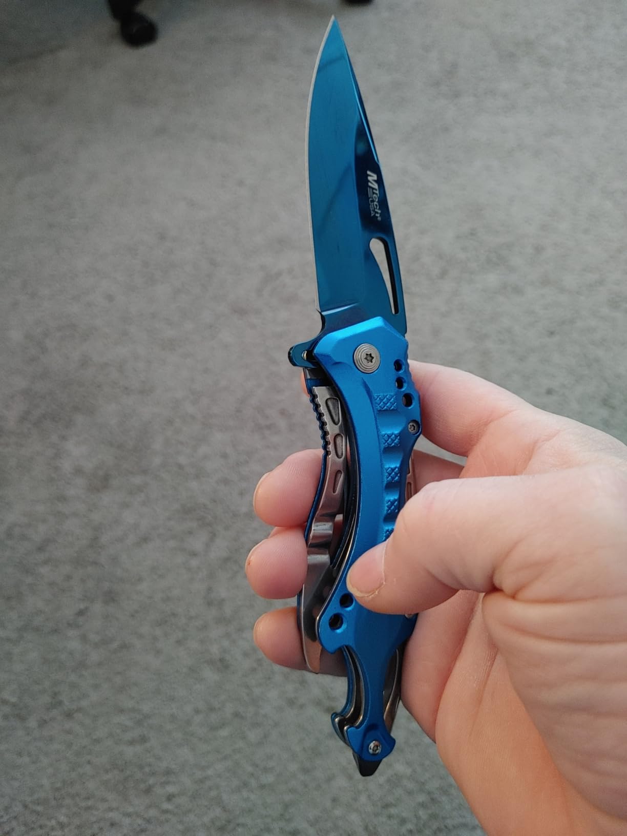 Blue MTech USA Ballistic folding knife held closed in a hand with the blade open, showing the contoured aluminum handle