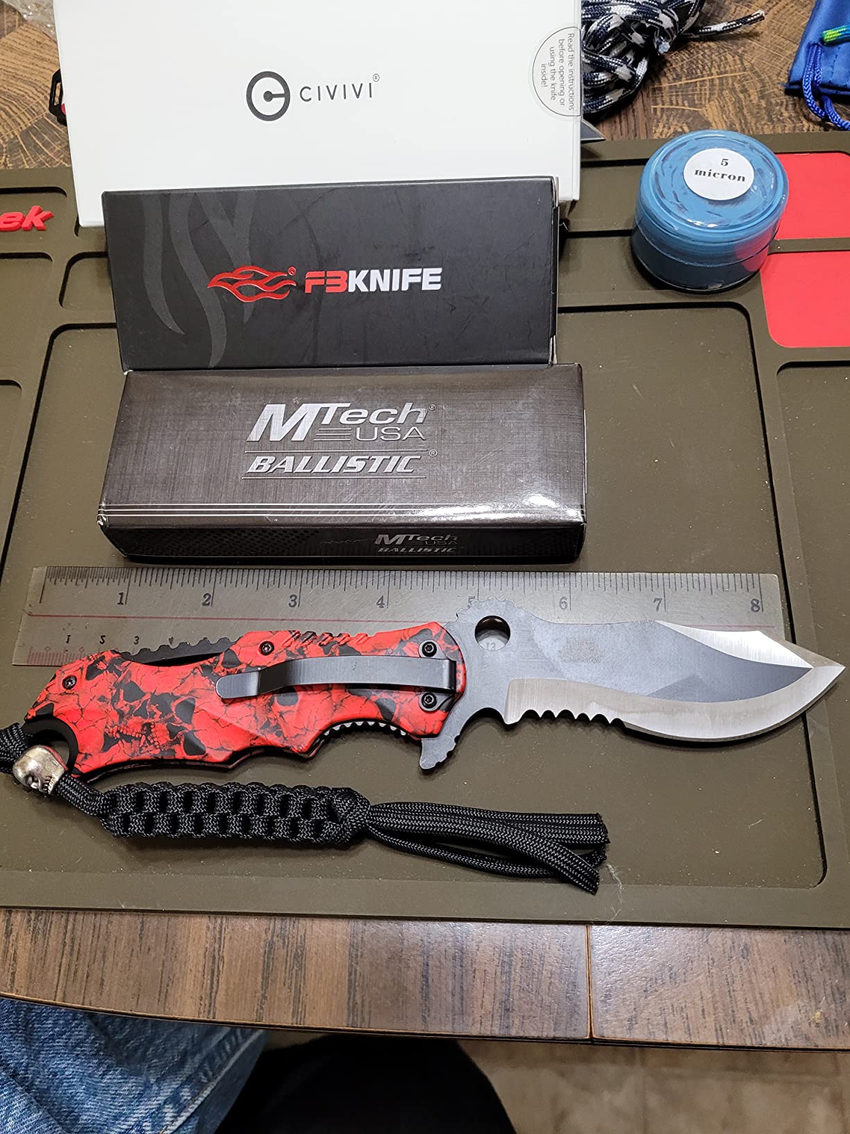 Red skull-pattern MTech USA Ballistic folding knife measured against a steel ruler at roughly eight inches open, with its box behind it
