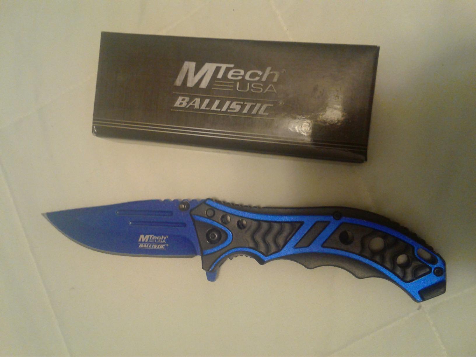 Blue MTech USA Ballistic folding knife lying beside its MTech USA Ballistic box on a white surface
